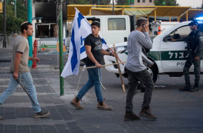 Photo: Israeli police escort Israeli right-wing settlers as they attack and clash with Palestinians in the city of Lod, 12 May 2021. Photo: Oren Ziv, Courtesy of Adalah www.Adalah.org